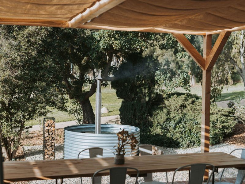Outdoor deck with wood-fired hot tub under trees at De Stilte.