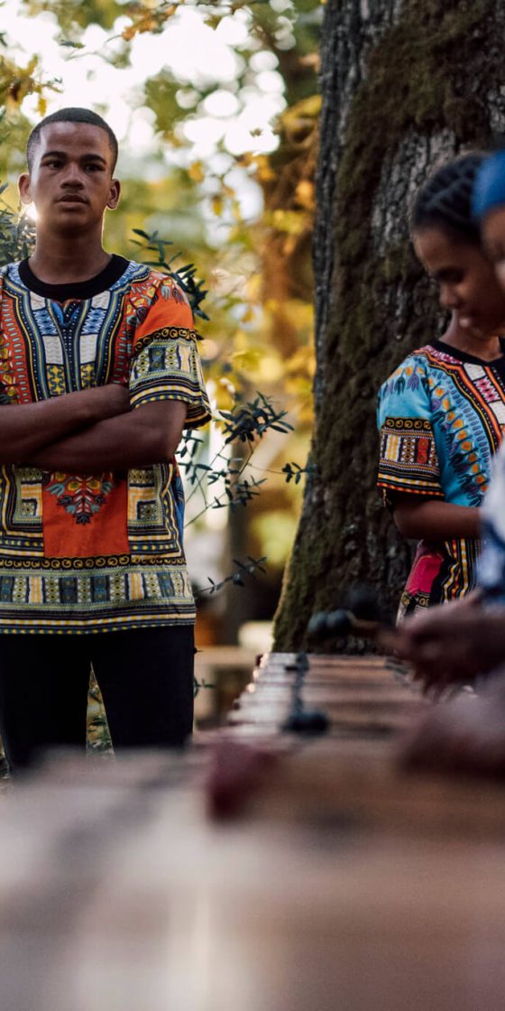 Guests dressed in traditional attire playing drums during an outdoor gathering at De Stilte