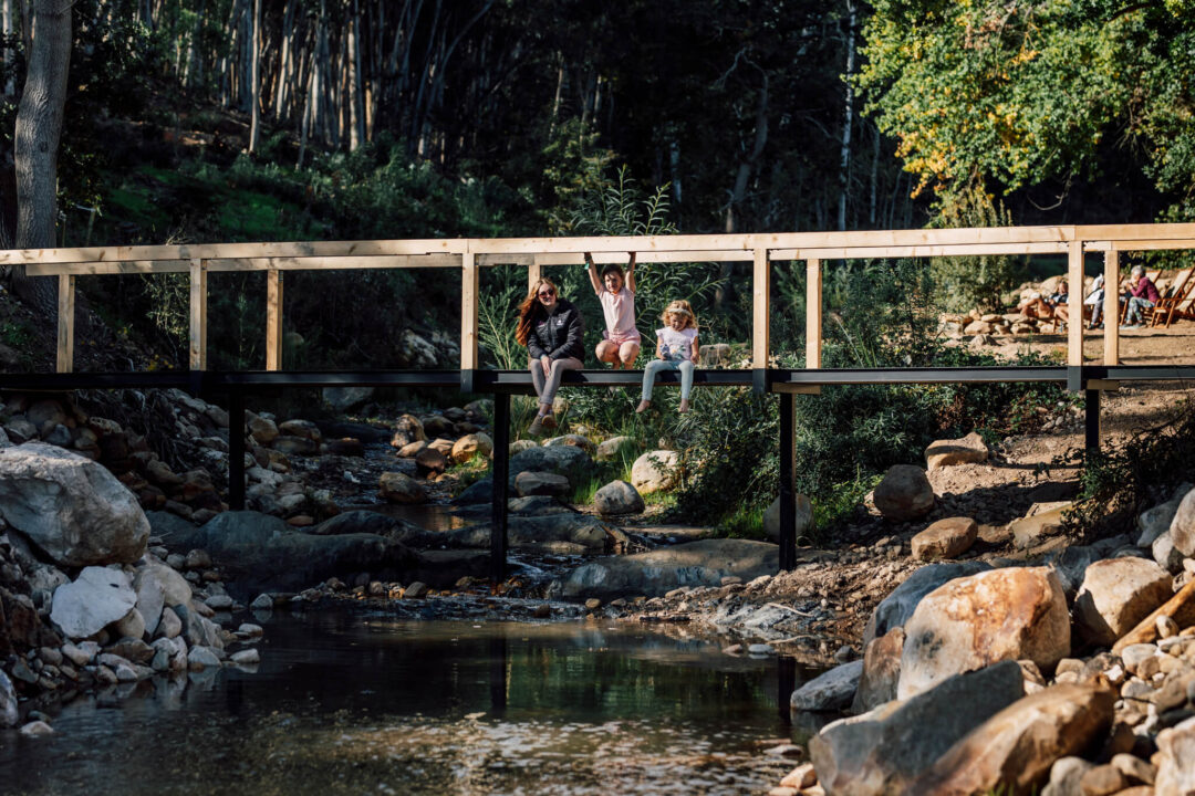 Footbridge over stream with guests seated on the bank